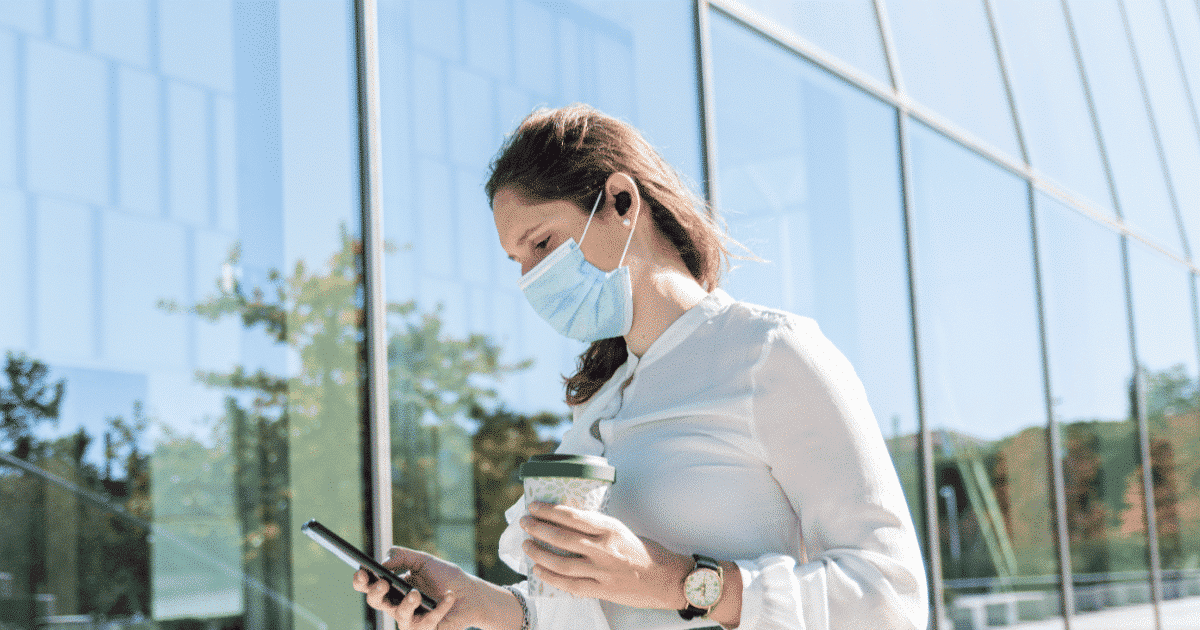 Frau mit Gesichtsmaske schaut auf ihr Handy