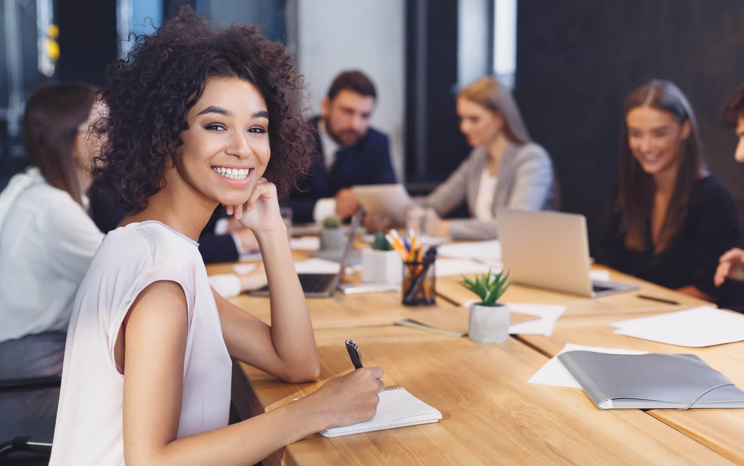 Collega's aan vergadertafel met dame die naar camera glimlacht